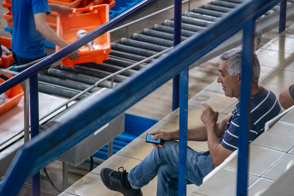 Crates moving along a conveyor while a manager checks his phone