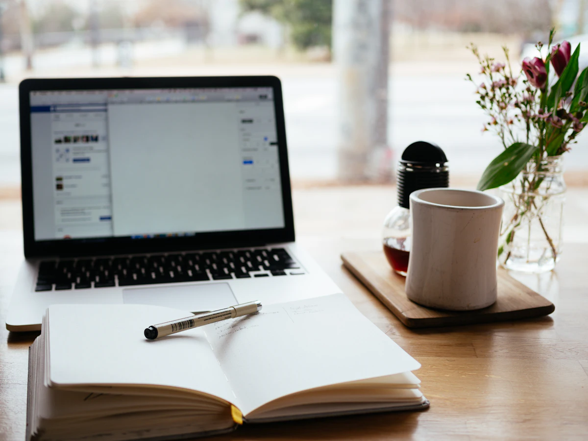 An open notebook, laptop and coffee on a wooden desk